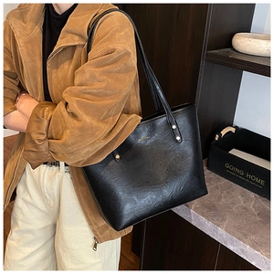 Close-up of black leather tote bag with subtle pebble texture and golden logo details