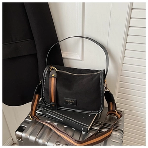 Detail of black canvas crossbody bag with leather trim and decorative wide strap
