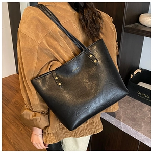 Detail of black faux leather tote with golden HOCOMU logo and decorative rivets