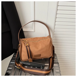 Detail view of brown suede underarm bag with wide striped strap on silver suitcase