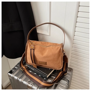 Close-up of brown suede square bag with striped fabric strap in a stylish office setting
