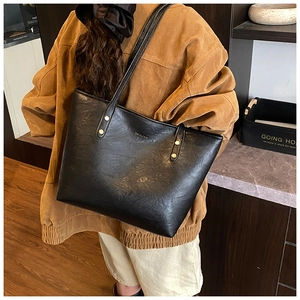 Detail of black tote bag featuring gold rivet accents and textured leather finish