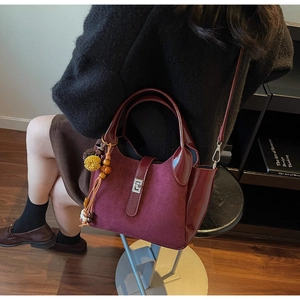 Close-up of burgundy frosted suede bucket bag with silver lock and yellow pompom charm