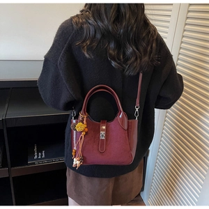 Detail of burgundy suede bucket bag with metal lock and vintage tassel charm on model