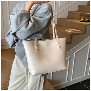 Detail of a beige tote bag with pleated texture and thin shoulder straps shown on a model