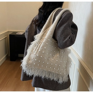 Close-up of knit tote bag featuring elegant pearl accents and soft feather fringe details