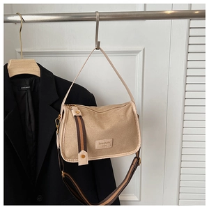 Close-up of beige rectangular shoulder bag with striped wide strap on a hanger