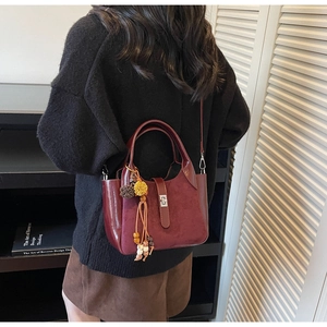 Detail of wine red bucket bag featuring leather suede patchwork and metal lock with pompom