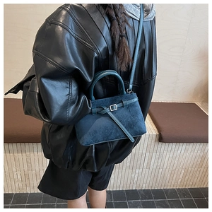 Detail of a dark blue matte suede bucket bag shown with metal buckle and shoulder strap