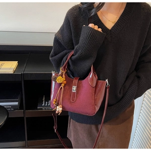 Detail of burgundy bucket bag with suede texture, silver lock and ethnic tassel pendant