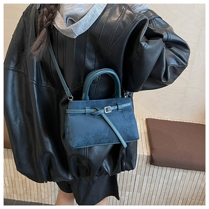 Detail of teal suede bucket bag with decorative buckle and rounded top handle