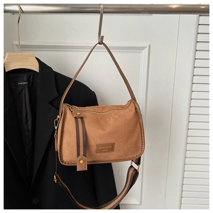 Detail of a brown suede crossbody bag showing textured fabric and striped strap