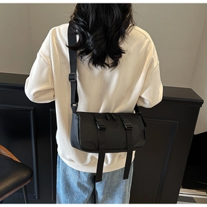 Detail view of black cylinder crossbody bag with buckle straps and wide shoulder strap