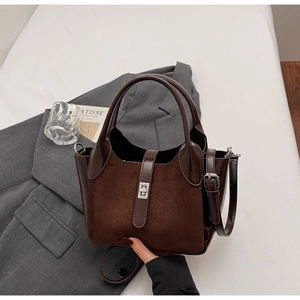 Detail of dark brown matte and patent leather bucket bag on grey suit background