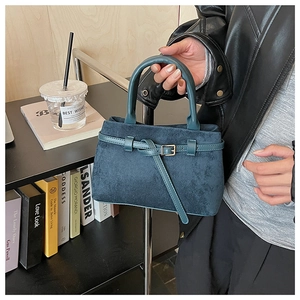 Detail of teal suede handbag with metal buckle and single handle in lifestyle setting