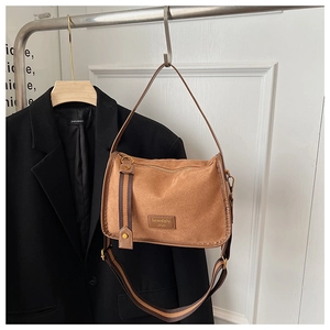 Close-up of brown suede crossbody bag with wide textile strap and zip closure