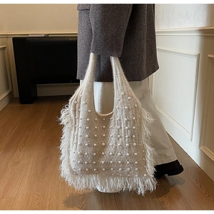 Detail of cream knit tote bag with delicate pearl accents and flowing fringe edges