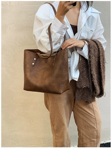 Detail of caramel brown retro tote bag with rivet accents and embossed logo on texture