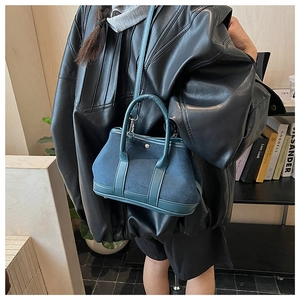 Detail of blue suede shoulder bag with leather trim held by model in leather jacket