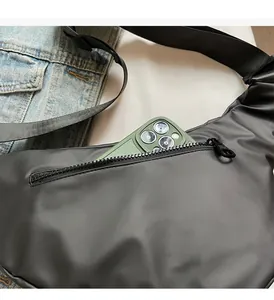 Detail view of black dumpling bag showing front zipper pocket with smartphone for scale