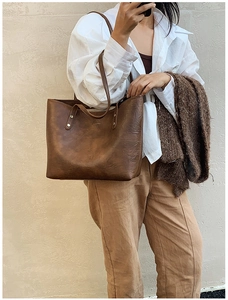 Macro view of vintage brown leather tote bag showing riveted handles and aged texture
