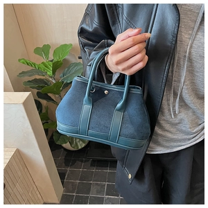 Detail of teal suede tote bag featuring smooth leather trim and metal clasp closure