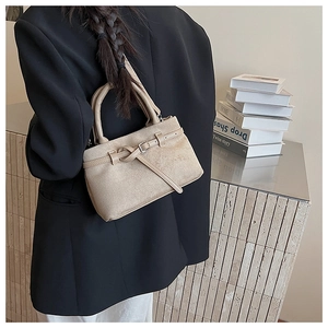 Detail view of a beige matte suede bucket bag worn over the shoulder by a model