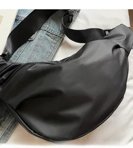 Detail of a minimalist black half-moon crossbody bag with nylon strap on denim background