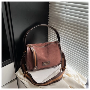 Detail of tan suede satchel with striped strap and vintage gold hardware on white books