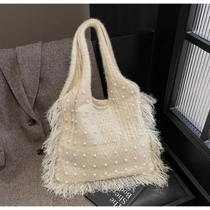 Detail of cream knit tote bag with pearl accents and fluffy feather trim on a coat