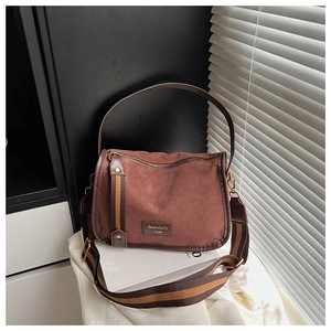 Close-up of brown suede crossbody bag with wide striped strap and metal logo on a magazine