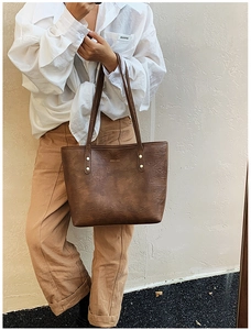 Detail of vintage brown textured leather tote bag with golden logo and slim handles