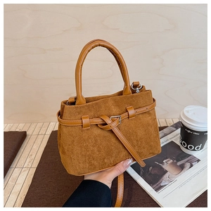 Detail of caramel brown suede handbag with leather cylindrical handle and decorative strap
