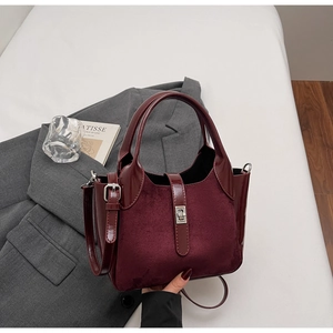Detailed texture of burgundy suede and glossy patent leather bucket bag on a suit