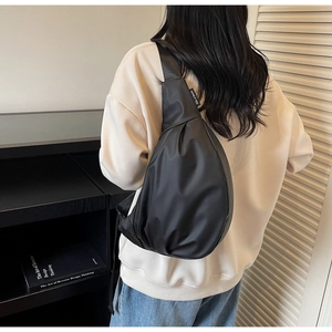 Detailed view of black nylon crossbody sling bag with brand tag on person wearing hoodie