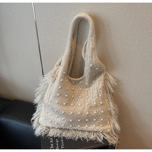 Close-up of beige knitted tote bag with faux pearls and elegant fringe tassels