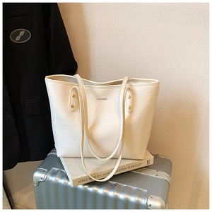 Detail of off-white faux leather tote bag with gold logo and rivet on silver suitcase