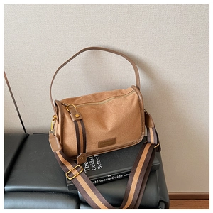 Detail of a brown crossbody bag with striped wide shoulder strap and metal zipper on books