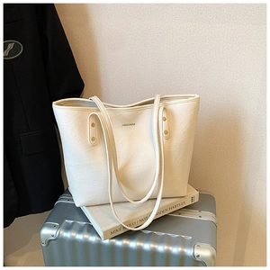 Detail of off-white faux leather tote bag with metal rivets and HOCOMU logo lettering