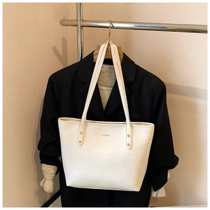 Detail of white leather tote bag with embossed MOCOMO logo and gold rivet fasteners