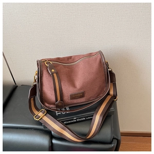 Detail of dark brown faux suede crossbody saddle bag with striped woven strap and logo