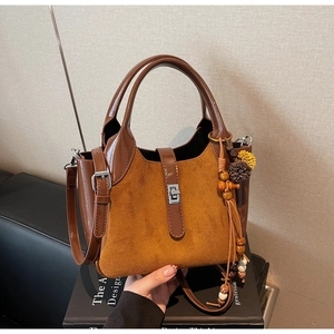 Detail of suede bucket bag with brown leather handle and ethnic style tassel charm