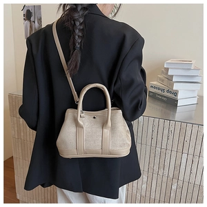 Detail of beige suede and leather bucket bag worn with a black blazer for a modern look