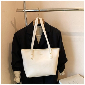 Detail of cream leather tote bag with lychee texture and gold rivet hanging on suit