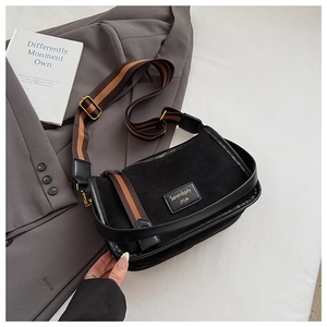 Detail of minimalist black crossbody bag with striped wide strap and leather logo patch