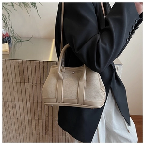 Detail of a beige suede commuter handbag with leather handles and a detachable shoulder strap