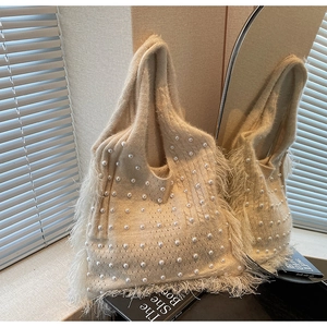 Close-up of beige knit tote bag featuring elegant pearl accents and soft feather fringe