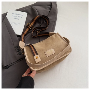 Detail of khaki suede crossbody bag featuring a striped wide shoulder strap on grey blazer