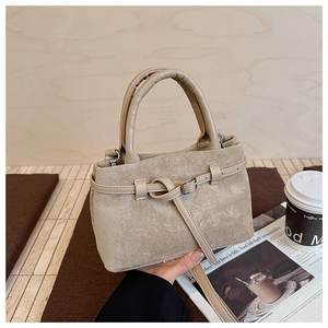 Detail of matte suede texture and leather strap with silver buckle on a beige bucket bag