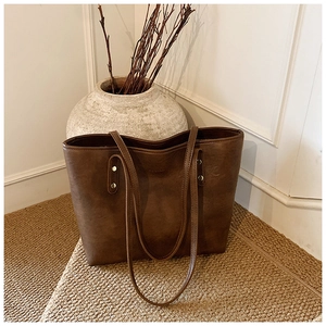 Detailed view of deep brown tote bag featuring matte PU leather and metal rivet details